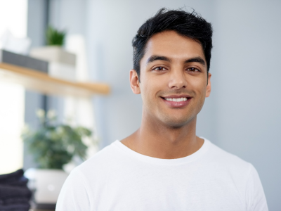 Man smiling at the camera in a white t-shirt, indoors with a blurred background.
